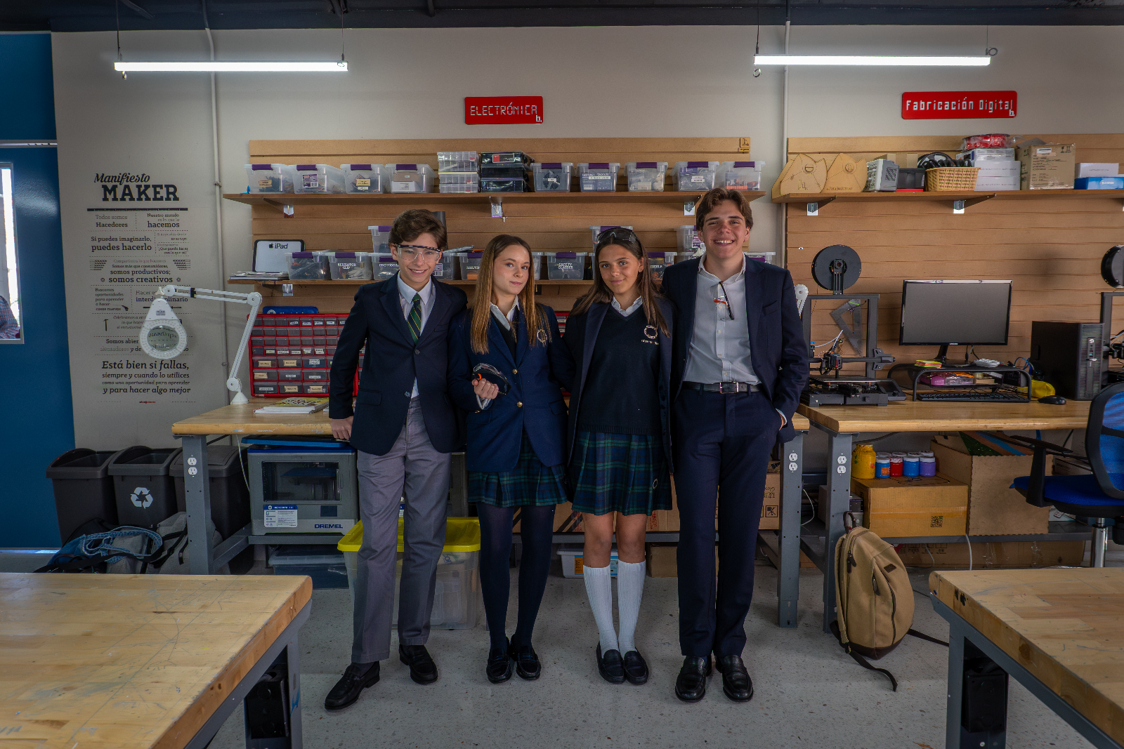 Cuatro estudiantes posan en un laboratorio de electrónica y fabricación digital con estantes de componentes detrás.